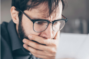 Homem branco, de óculos com bordas pretas, tem olhar atônito ao observar folha de pagamentos e percebe quando as apostas viram um vício